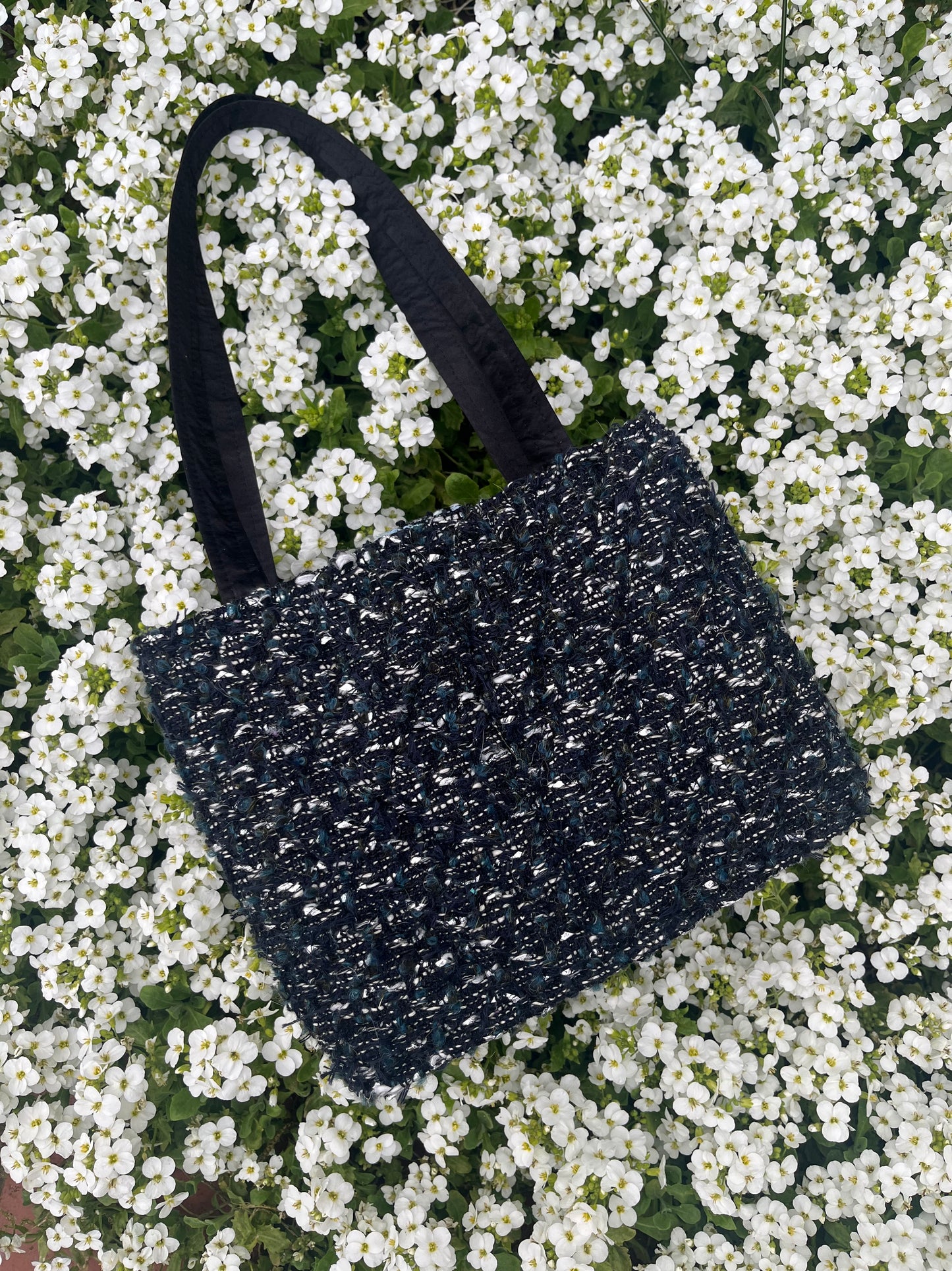 The Lindisfarne medium-sized handbag in rich sustainable tweed, finished with structured satin handles and sleek metal detailing.