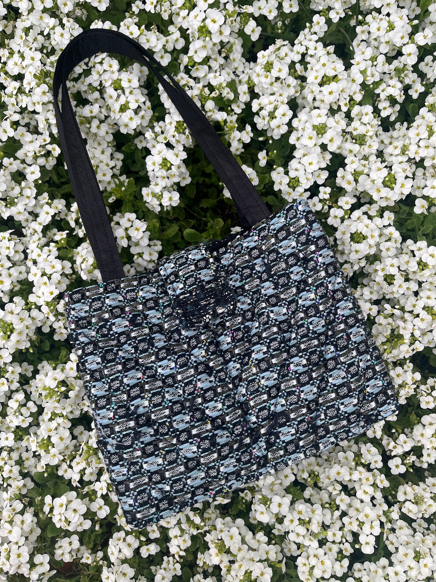 The Lindisfarne medium-sized handbag in rich sustainable tweed, finished with structured satin handles and sleek metal detailing.