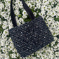 The Lindisfarne medium-sized handbag in rich sustainable tweed, finished with structured satin handles and sleek metal detailing.