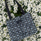The Lindisfarne medium-sized handbag in rich sustainable tweed, finished with structured satin handles and sleek metal detailing.