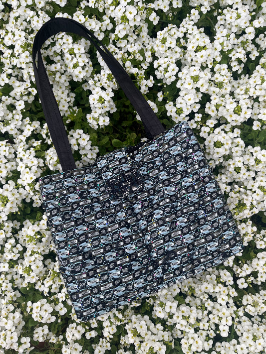 The Lindisfarne medium-sized handbag in rich sustainable tweed, finished with structured satin handles and sleek metal detailing.
